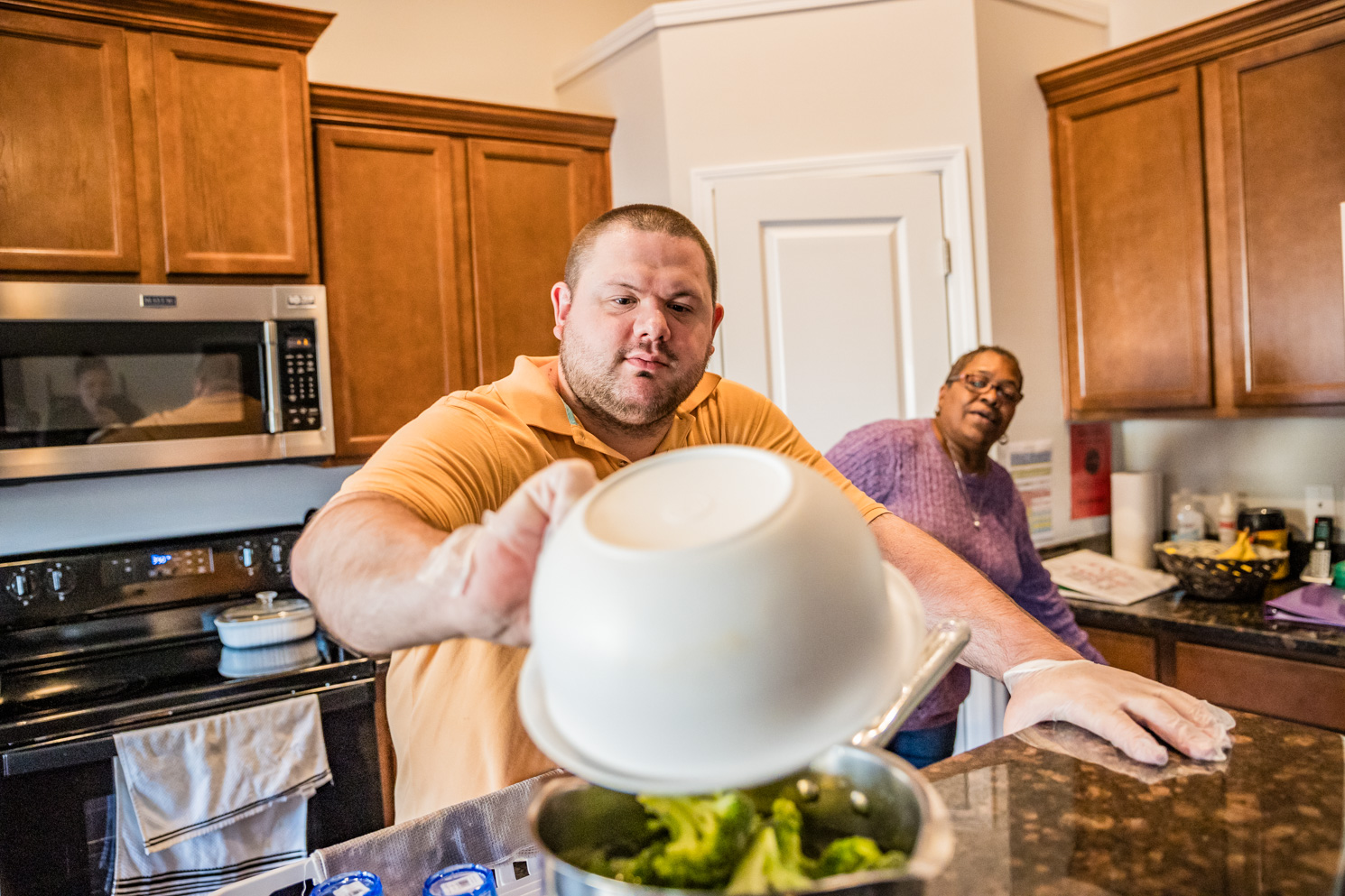 A residential services volunteer assists a Unity Bay member in the kitchen while both are cooking.